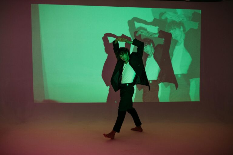 A male dancer poses dynamically with a colorful projection in a studio.