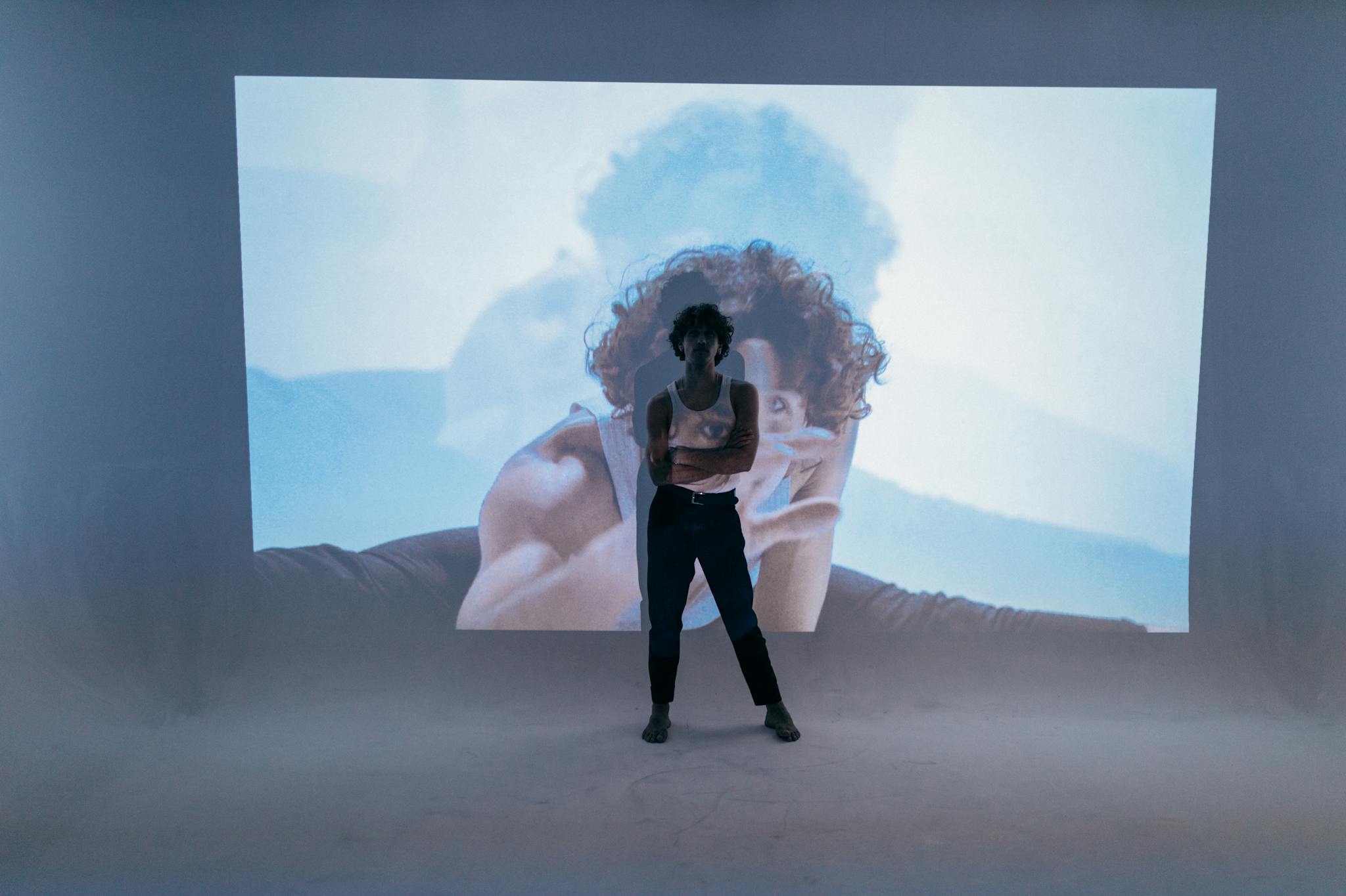 A stylish man poses in front of a vivid dance projection in a modern studio setting.