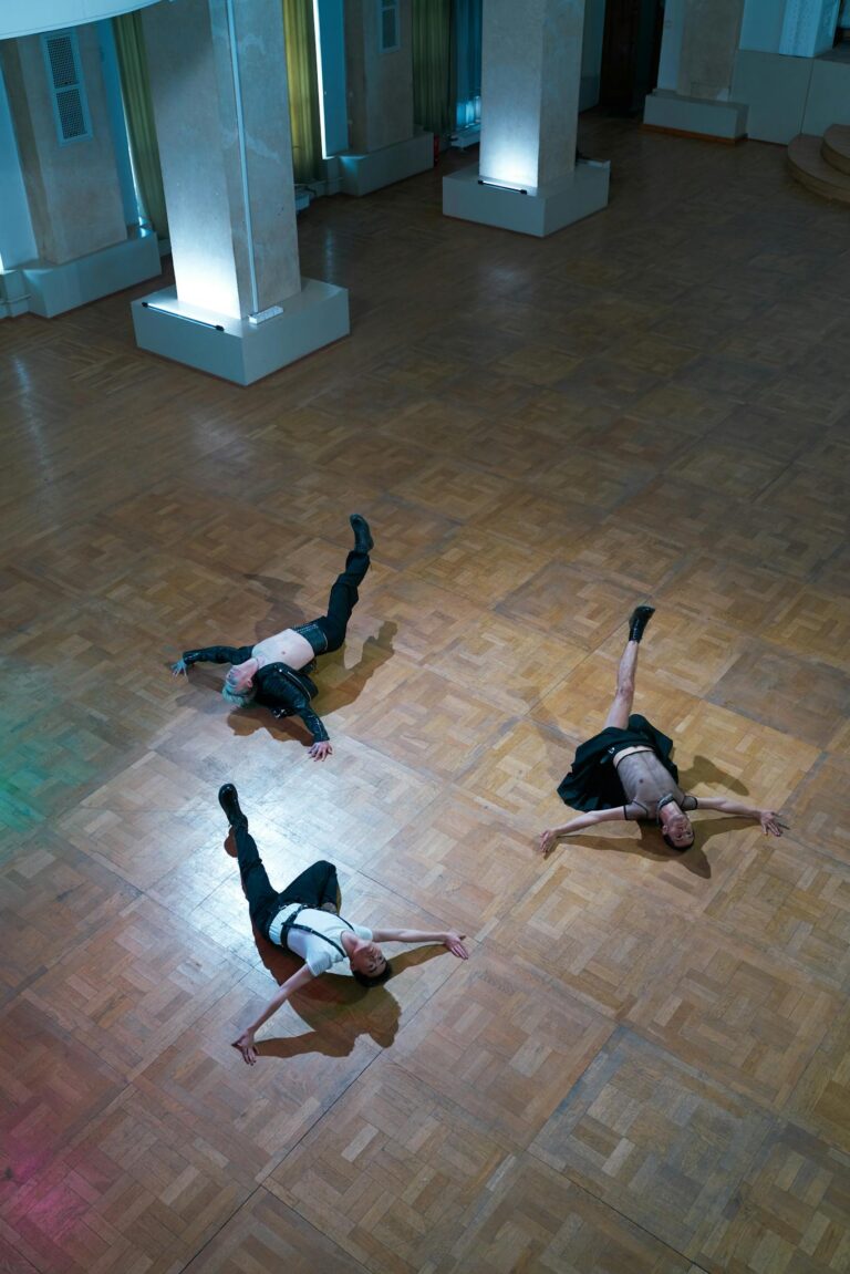 Three male dancers performing a contemporary routine on a wooden studio floor.